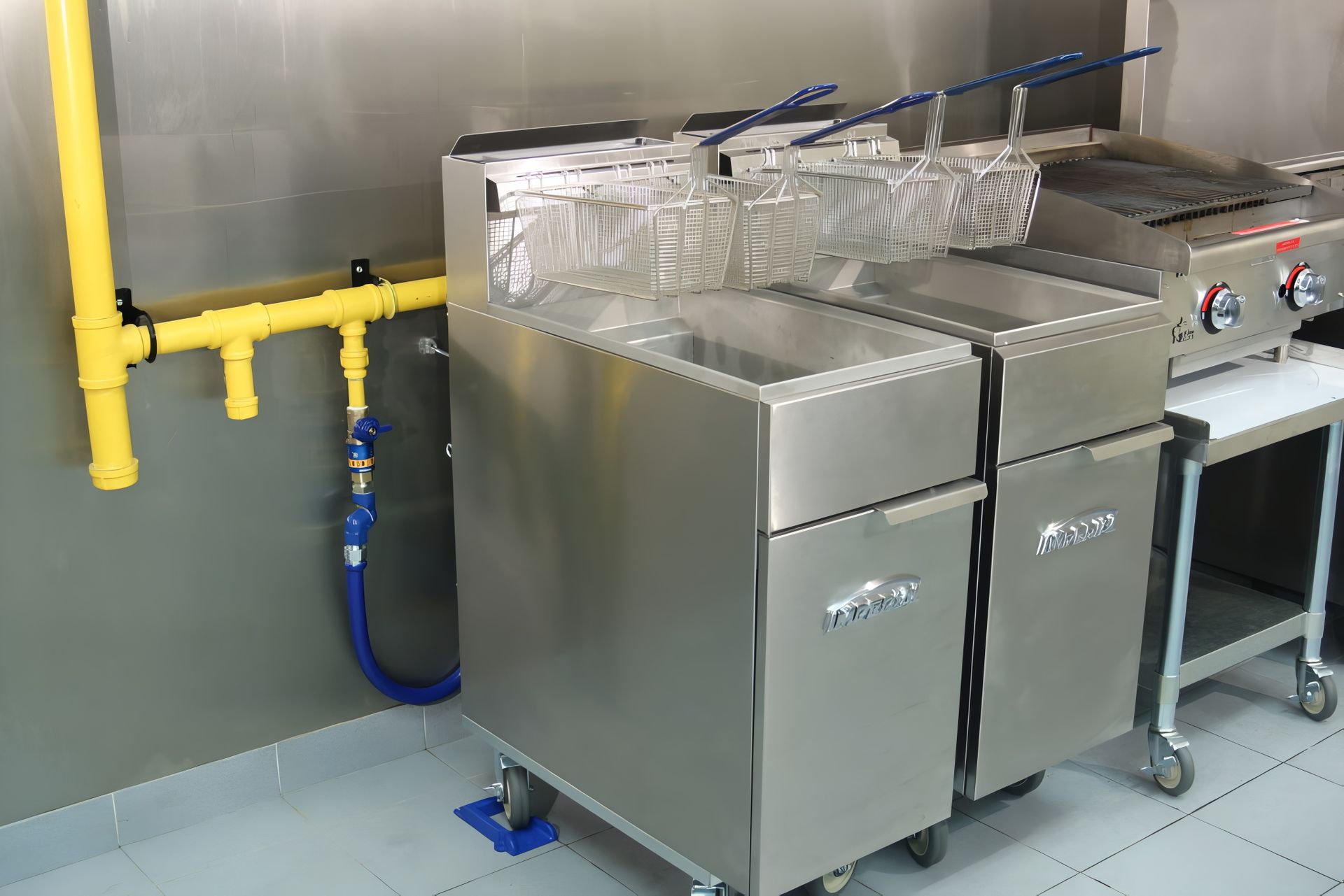 Two stainless steel commercial deep fryers in a kitchen. Yellow gas line visible.