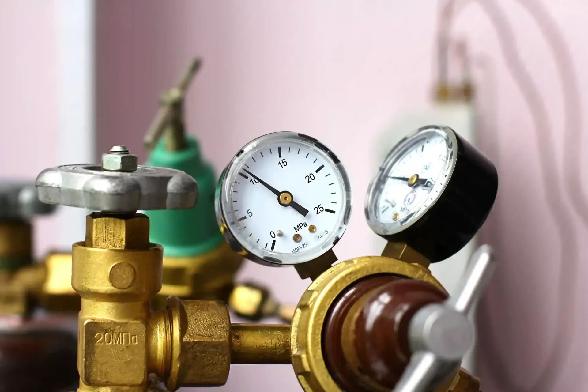 Close-up of brass gas regulator with two gauges, showing pressure levels. Background is pink and white.