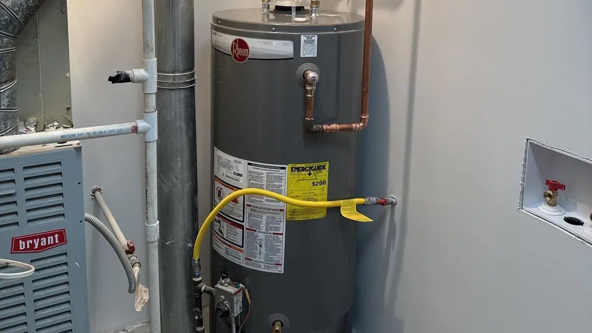 Gray water heater with yellow gas line and copper pipes in a utility closet
