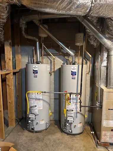 Two water heaters in a basement utility room with exposed ductwork and pipes.