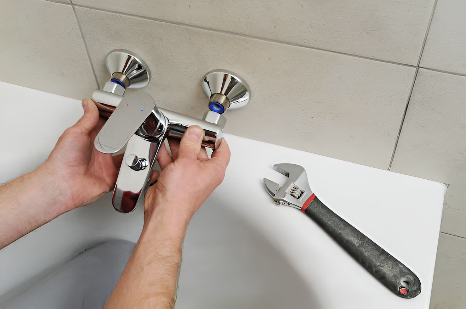 Person installing a chrome faucet on a white surface, with a wrench nearby.