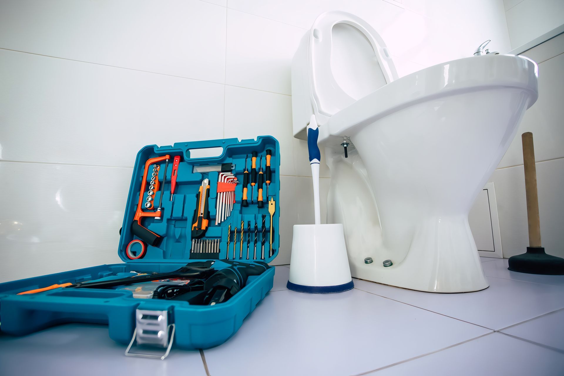 Open toolbox with tools beside a white toilet and plunger in a bathroom.