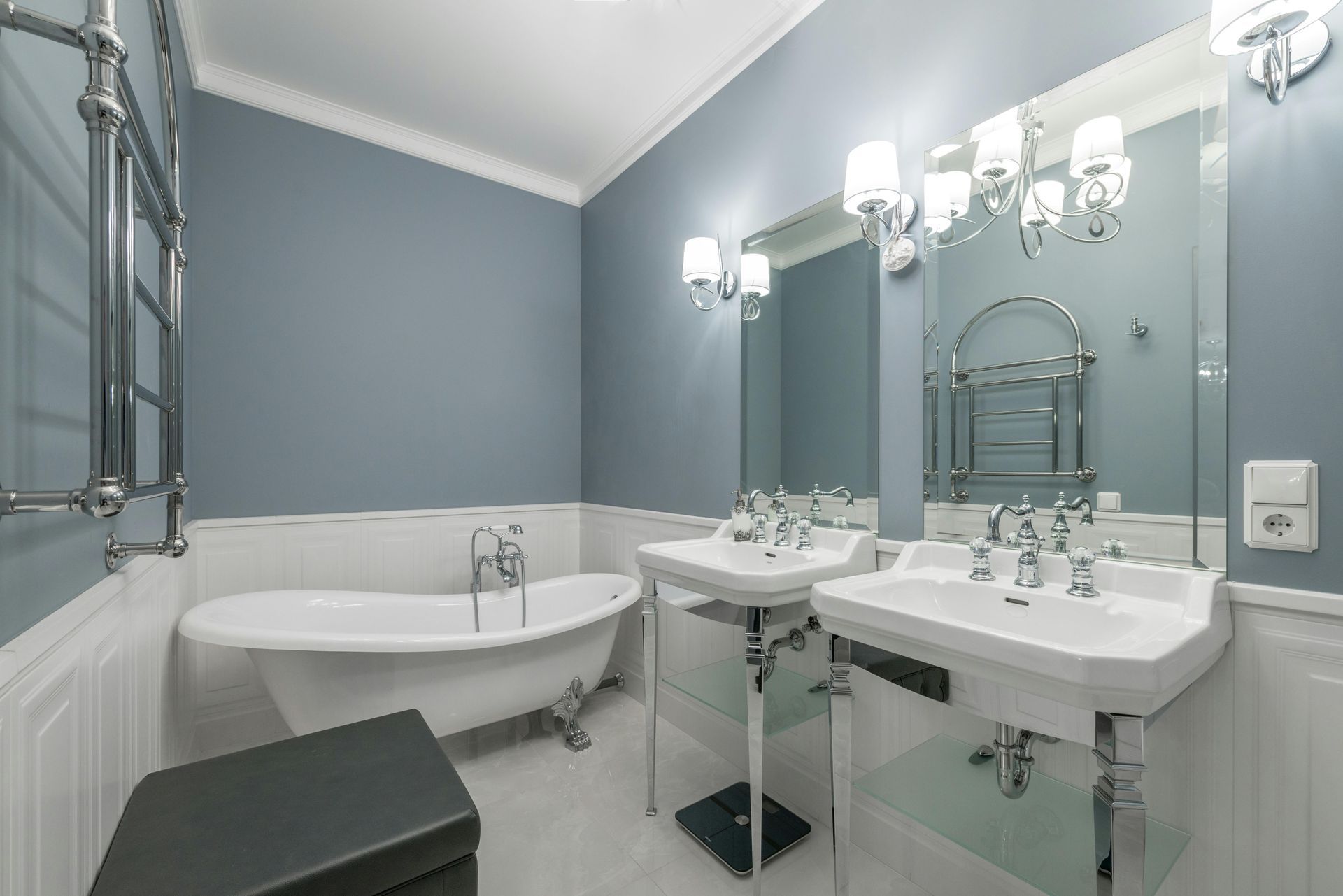Elegant bathroom with a blue wall and white trim. Features a clawfoot tub, pedestal sinks, and a large mirror