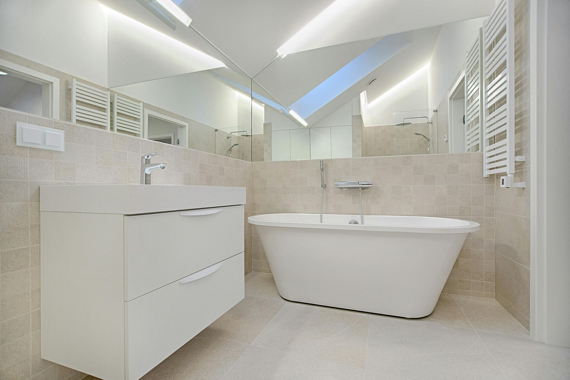 Modern bathroom with a white bathtub, vanity, and beige tiled walls. Large mirror above the vanity