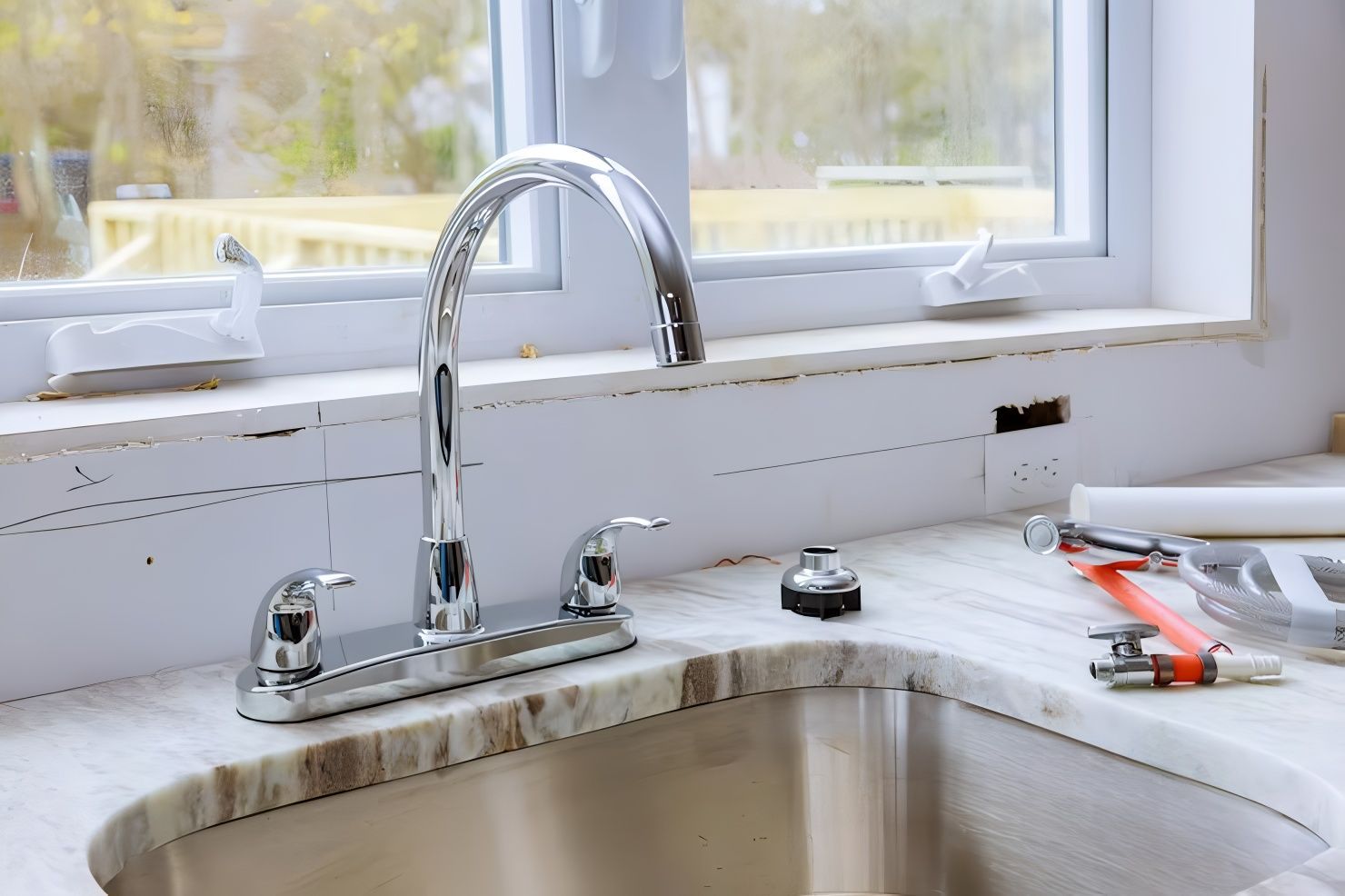 Chrome faucet installed in a kitchen sink with a marble countertop, window in the background, and tools nearby.