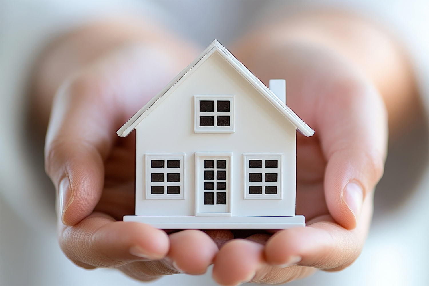 A person is holding a small white house in their hands.
