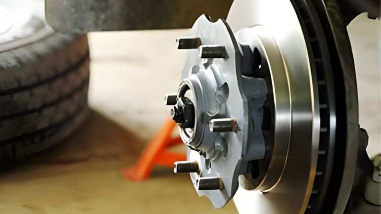 Close-up of a vehicle's wheel hub and brake rotor assembly with wheel studs, positioned on a shop floor.