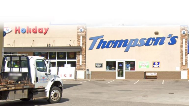 A white tow truck parked in front of a tan commercial building labeled