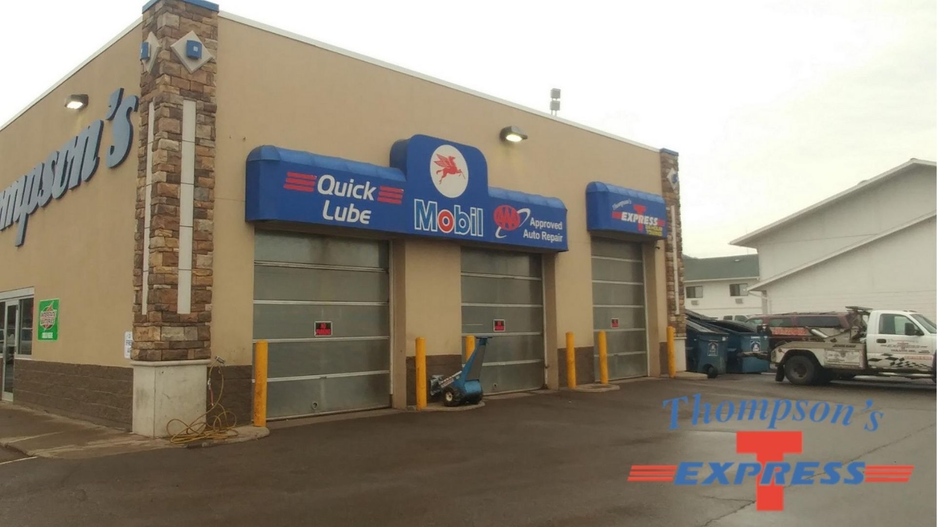 A tan, single-story Mobil automotive service building with three closed glass garage bays and an adjacent truck.