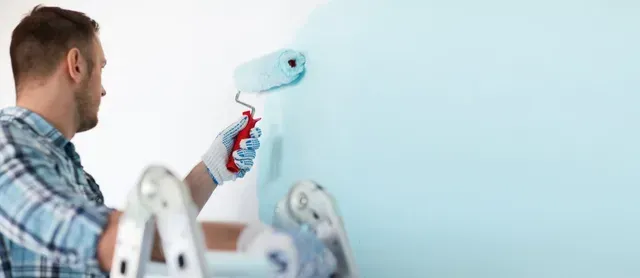 Professional painter applying light blue paint to an interior wall in Hattiesburg, MS.