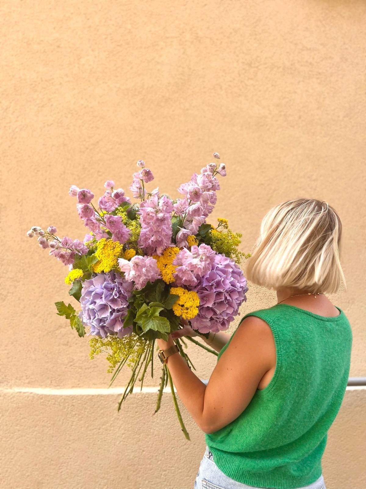 Une femme en débardeur rose tient un gros bouquet de fleurs.