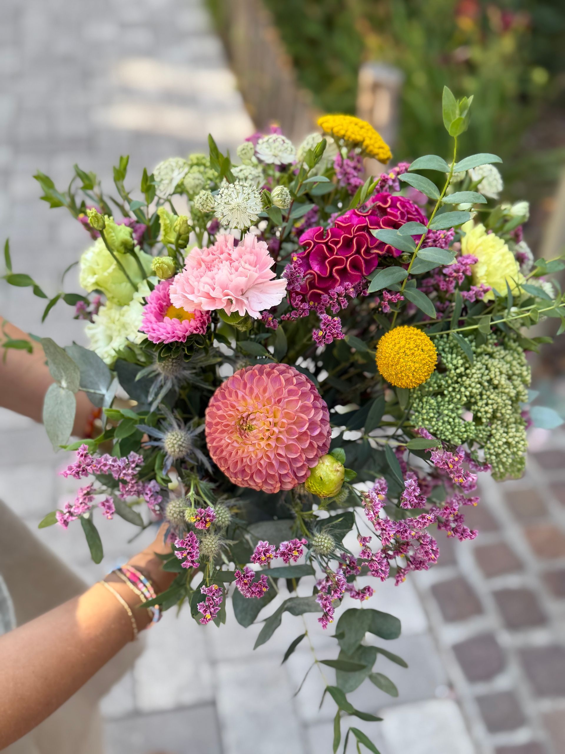 Une femme tient un bouquet de fleurs roses et jaunes.