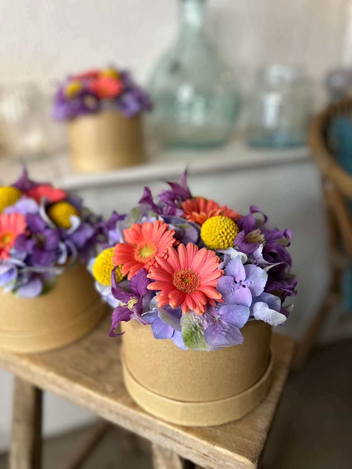Des compositions de fleurs séchées colorées dans des boîtes dorées sur un plateau en bois rustique