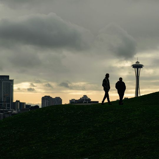 Two people walking on a grassy hill in front of a city skyline
