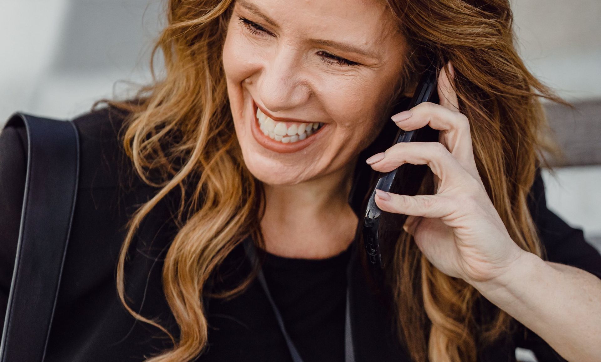 A woman is smiling while talking on a cell phone.
