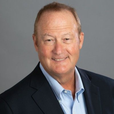 Portrait of a smiling man in a dark suit and light blue shirt against a gray background