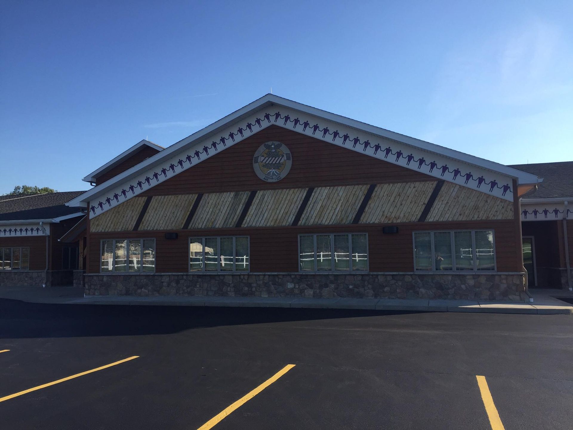 Brick storefront with a peaked roof and windows, seen across an empty parking lot under a clear blue sky