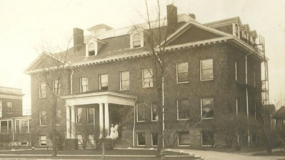 Sepia-toned historic brick building with a porch, dormer windows, and a small car parked outside
