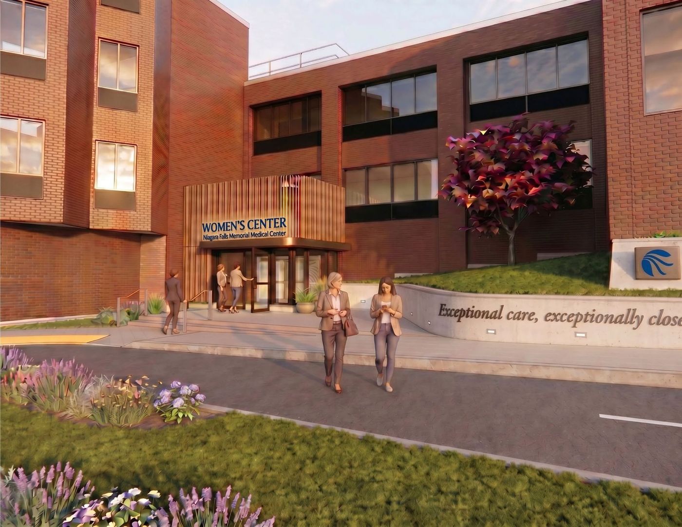 Modern brick hospital entrance with people walking, flower beds, and a sign reading “Empathetic care, compassionately close.”