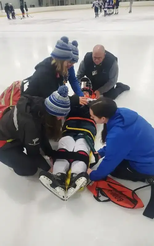 People helping an injured ice skater on the rink, with first aid being provided.