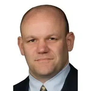 Head-and-shoulders portrait of a man in a dark suit and light blue shirt on a white background