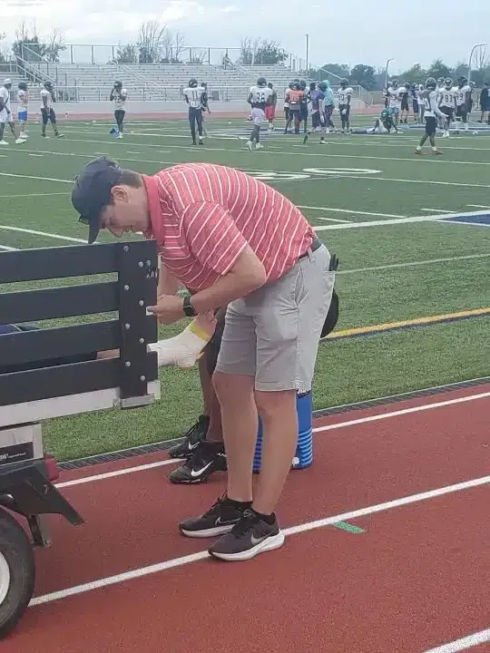 Person in red striped shirt bends over beside a wheelchair on a track field during a sports event.