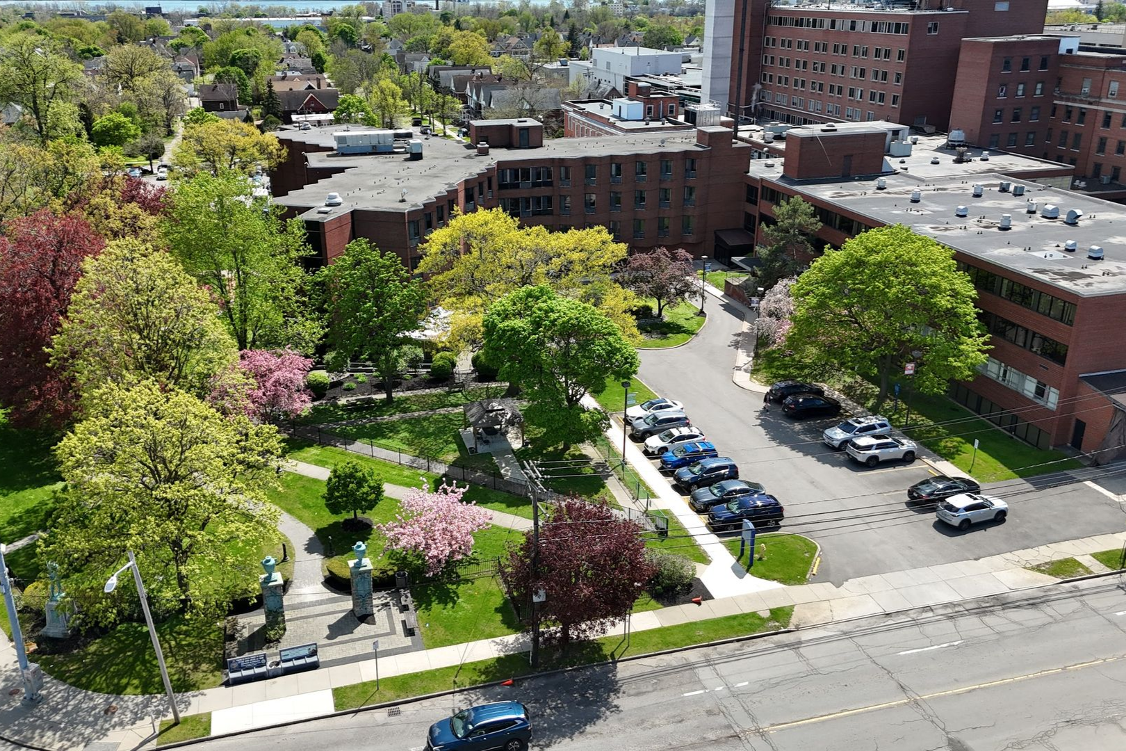 Aerial view of a green campus courtyard with trees, walking paths, parked cars, and brick buildings.