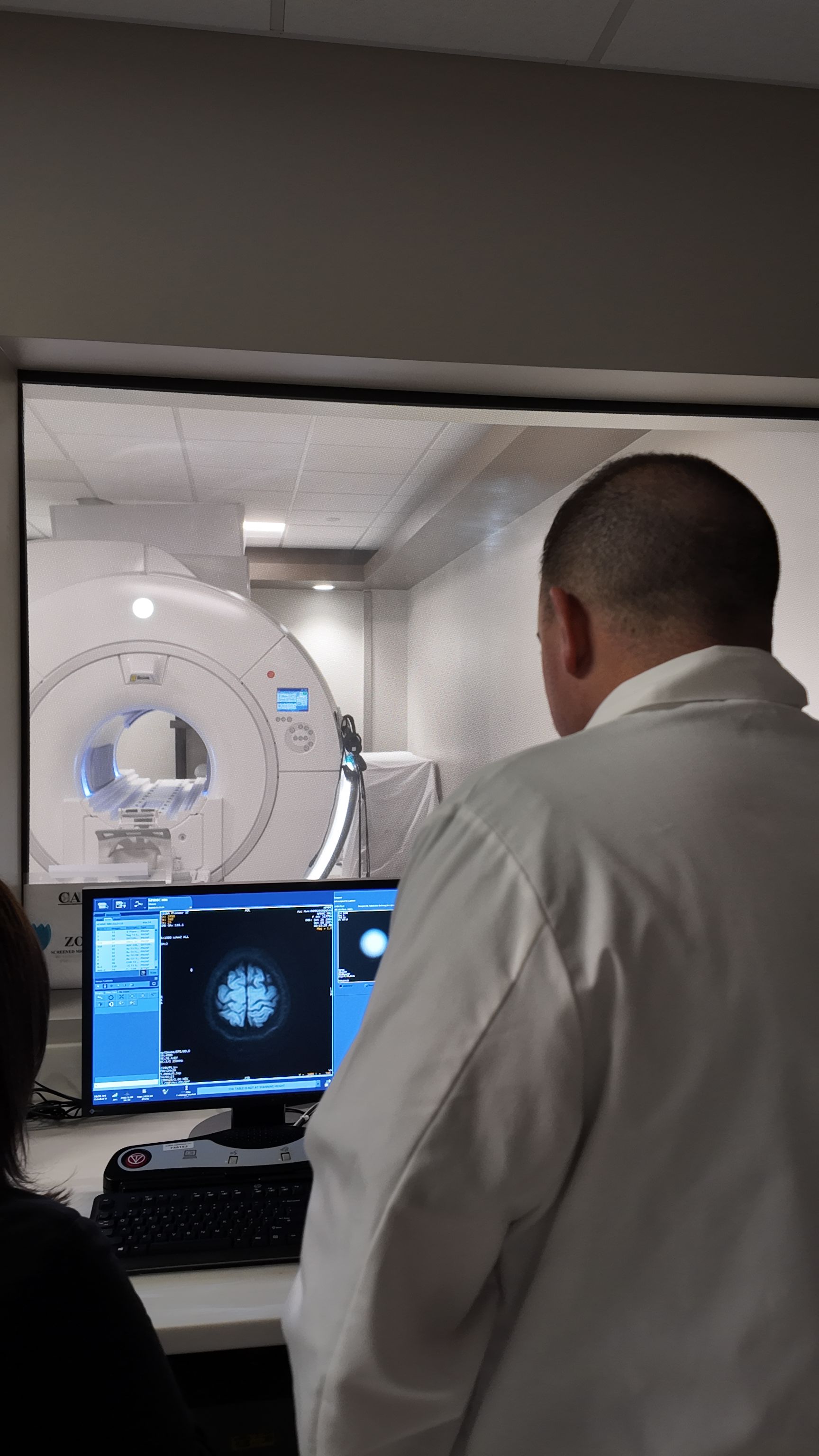 Doctor viewing brain scan images in a control room beside a large MRI scanner
