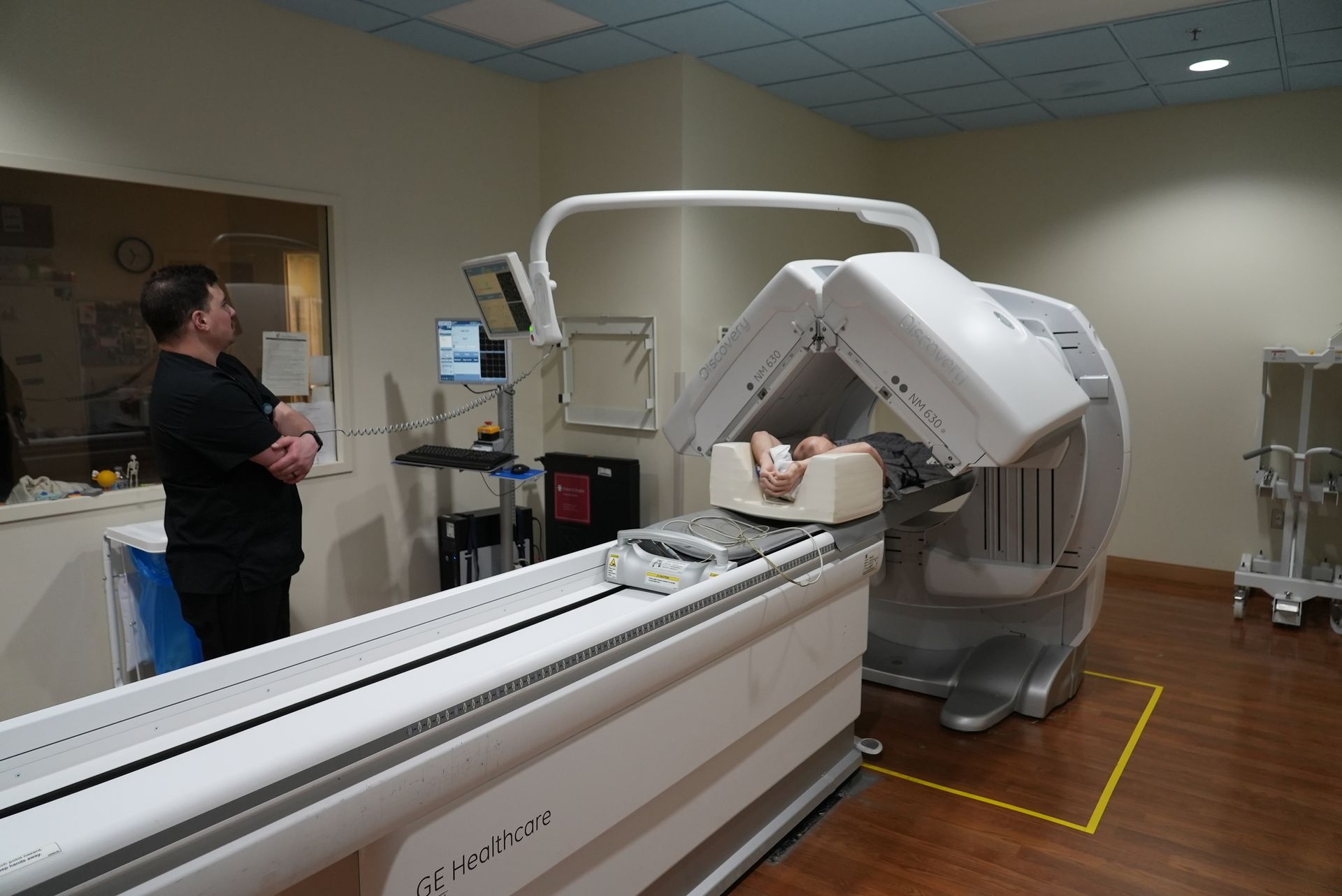 Patient in MRI scanner while technician stands nearby in a hospital imaging room