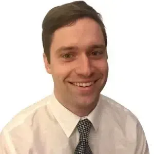 Smiling man in a white shirt and patterned tie against a plain white background
