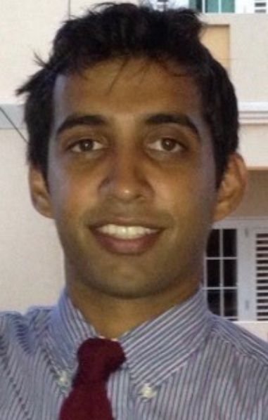 Portrait of a smiling person in a striped shirt and red tie, standing outdoors near a building.