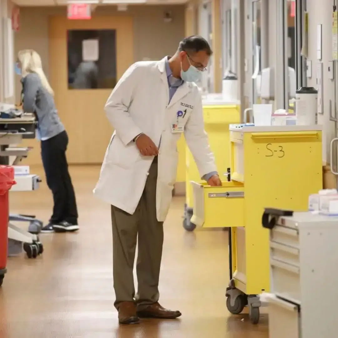 Doctor in white coat checking a yellow cart in a hospital hallway