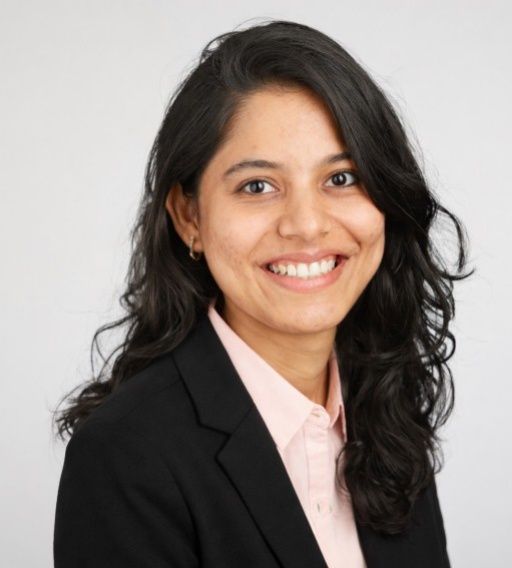 Smiling person in a black blazer and light pink shirt against a white background
