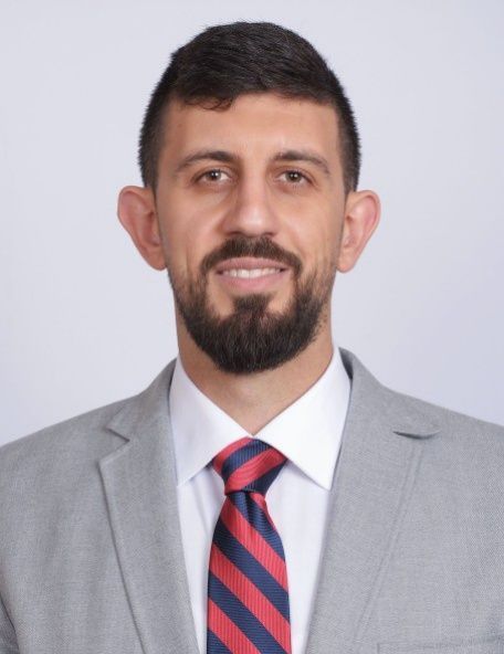 Portrait of a smiling man in a gray suit, white shirt, and red-and-blue striped tie.