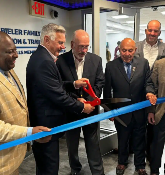 Men in suits cut a blue ribbon at a building opening ceremony.