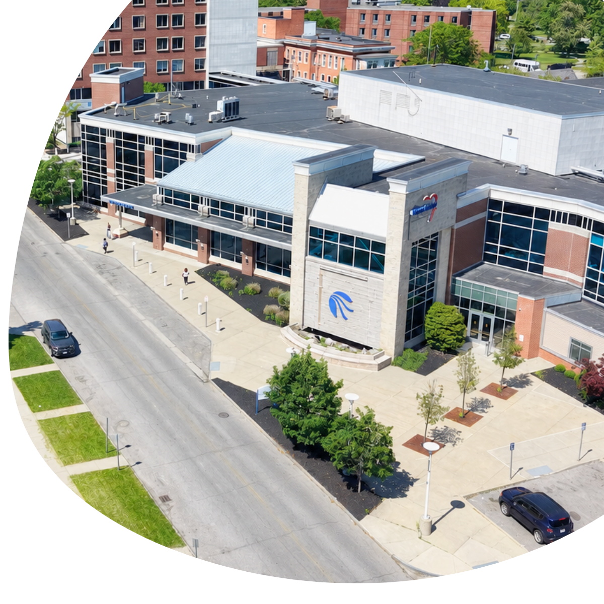 Aerial view of a modern brick and glass building beside a street with sidewalks and trees.