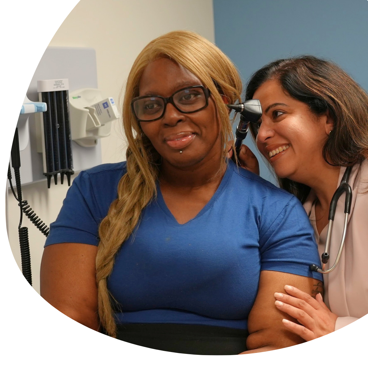 Woman in blue shirt smiling as a clinician checks her arm in a medical office