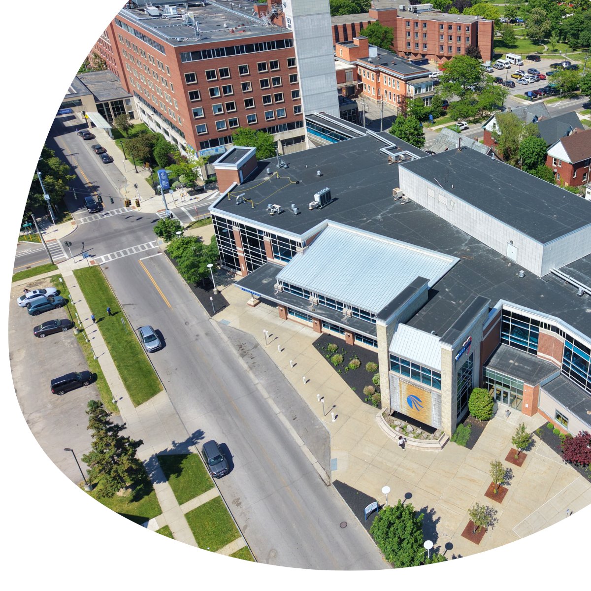 Aerial view of a city street beside a modern building with parked cars and a small plaza.