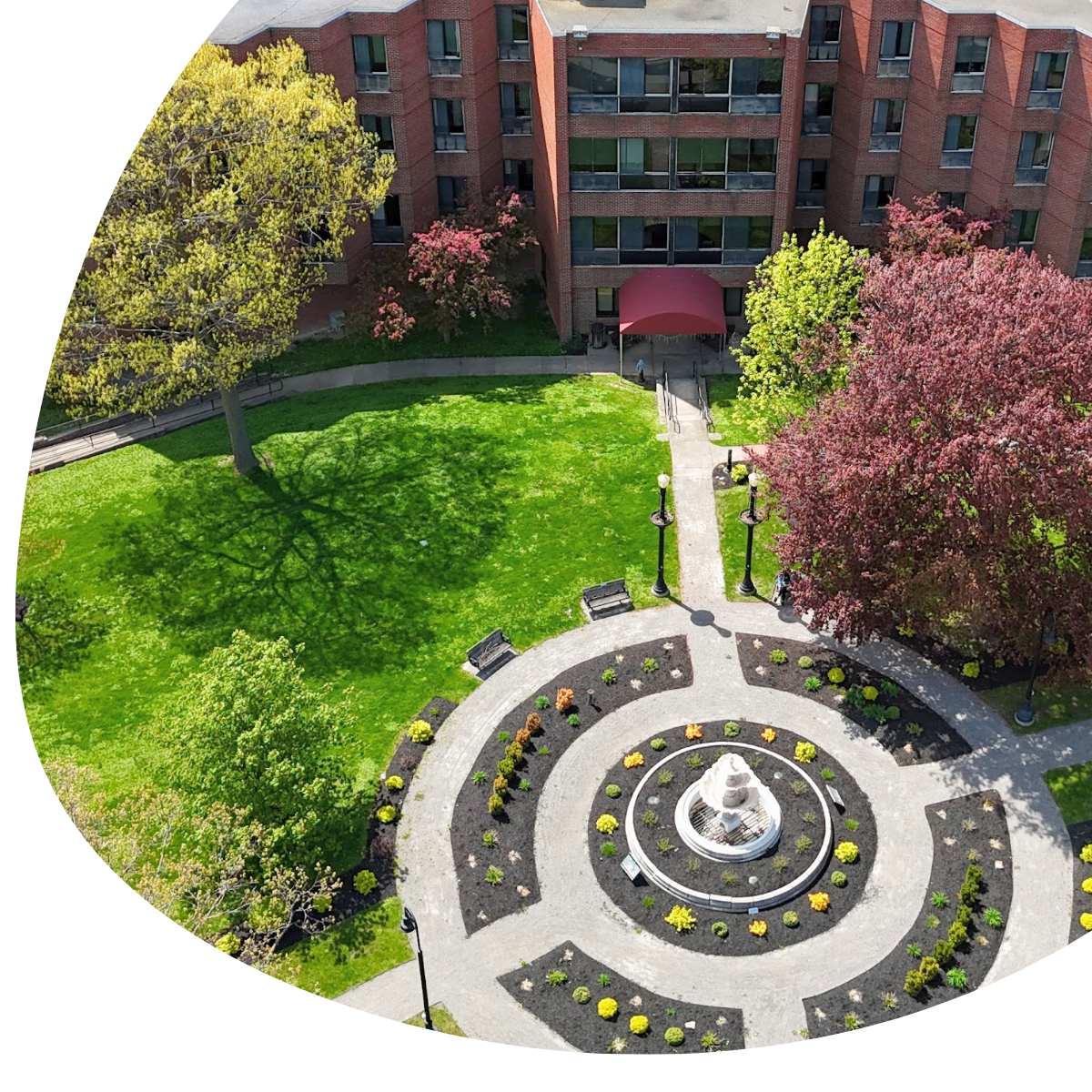 Courtyard with circular fountain, green lawn, and flowering trees beside a brick apartment building