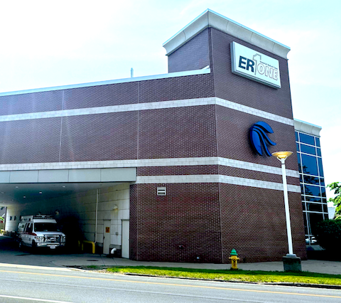 Brick ER hospital entrance with covered drop-off area and parked ambulance under a clear sky