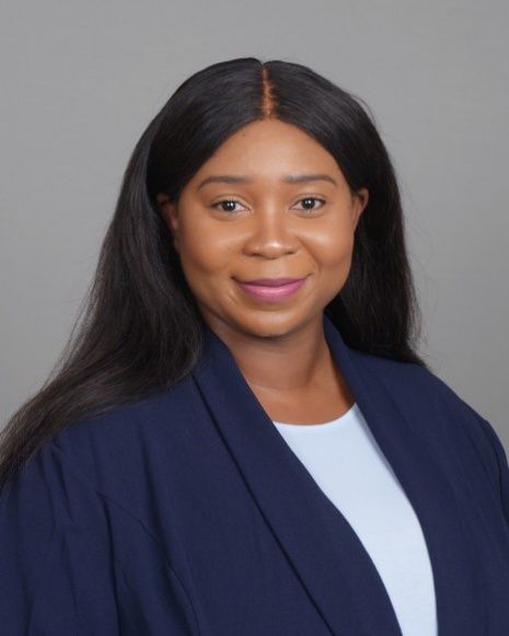 Portrait of a smiling person in a navy blazer against a gray background