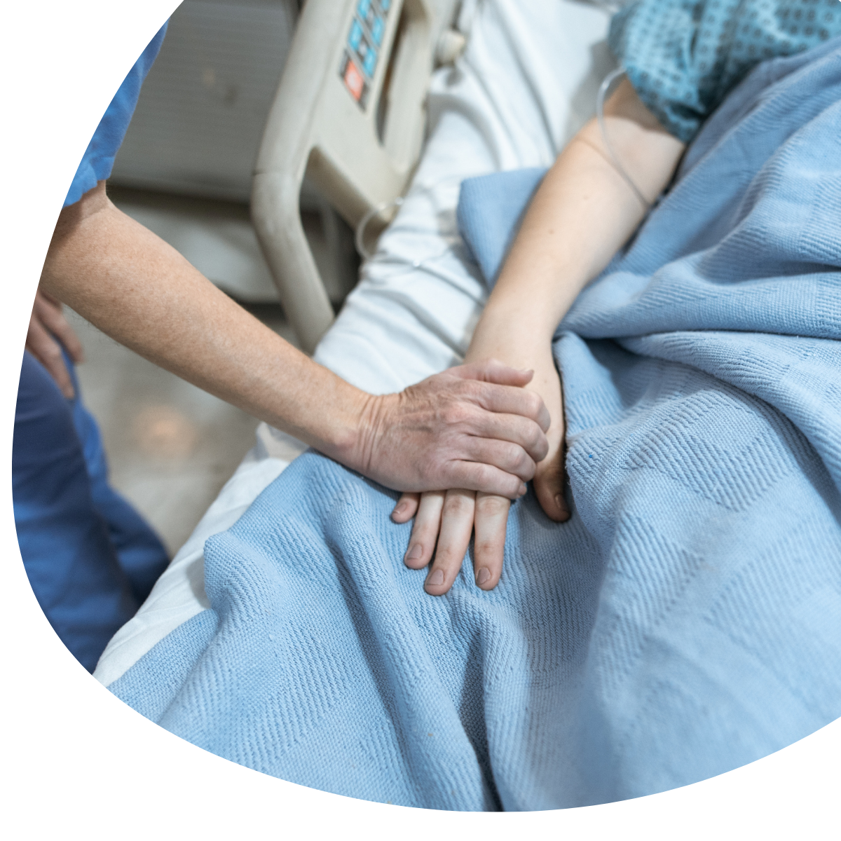Hand comforting a patient’s hand beside a blue hospital blanket