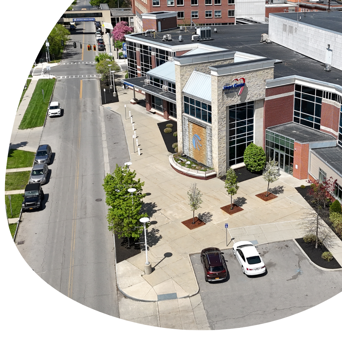 Aerial view of a city street beside a modern building with parked cars and a small plaza.