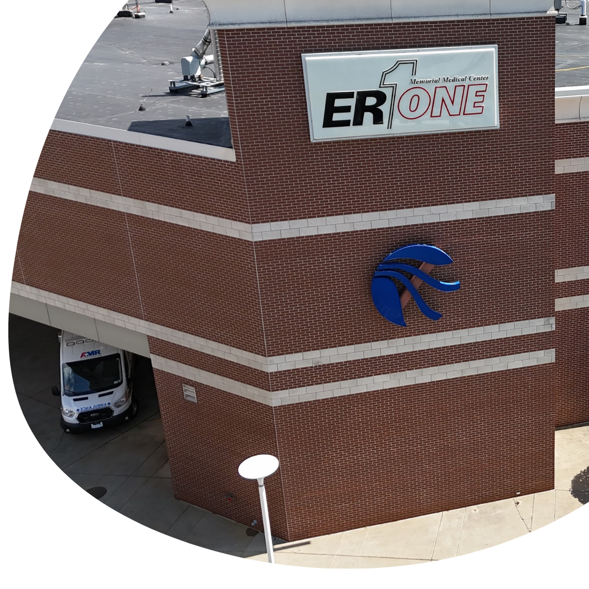Brick building with ER One sign and blue logo, viewed from above with parked vehicles below