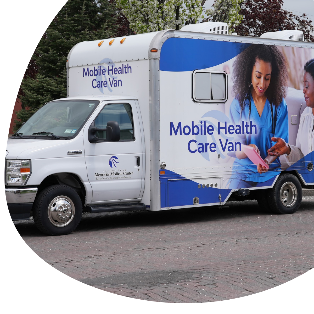 White mobile health care van with blue graphics and staff imagery parked outdoors