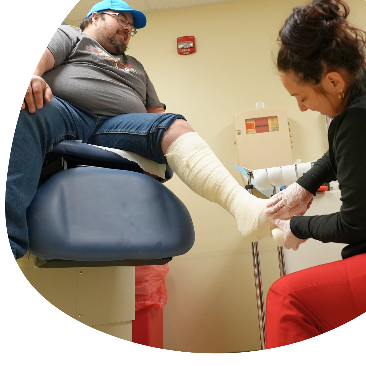 Clinician wraps a patient’s lower leg in a clinic exam room while he sits on an exam table.