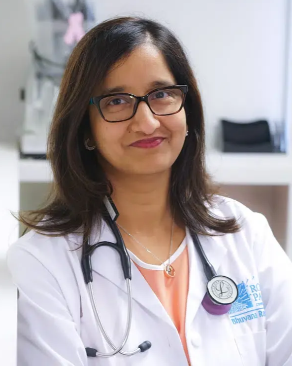Healthcare professional in a white coat and stethoscope, smiling in a clinic setting.