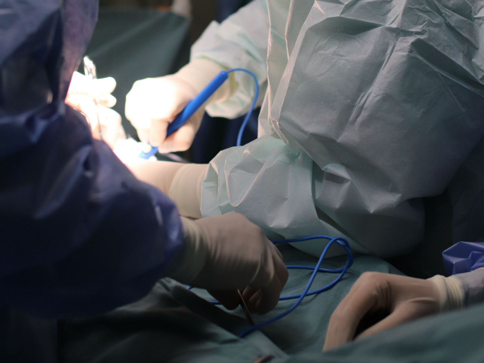 Surgeons in blue scrubs and gloves performing a procedure under bright operating room lights