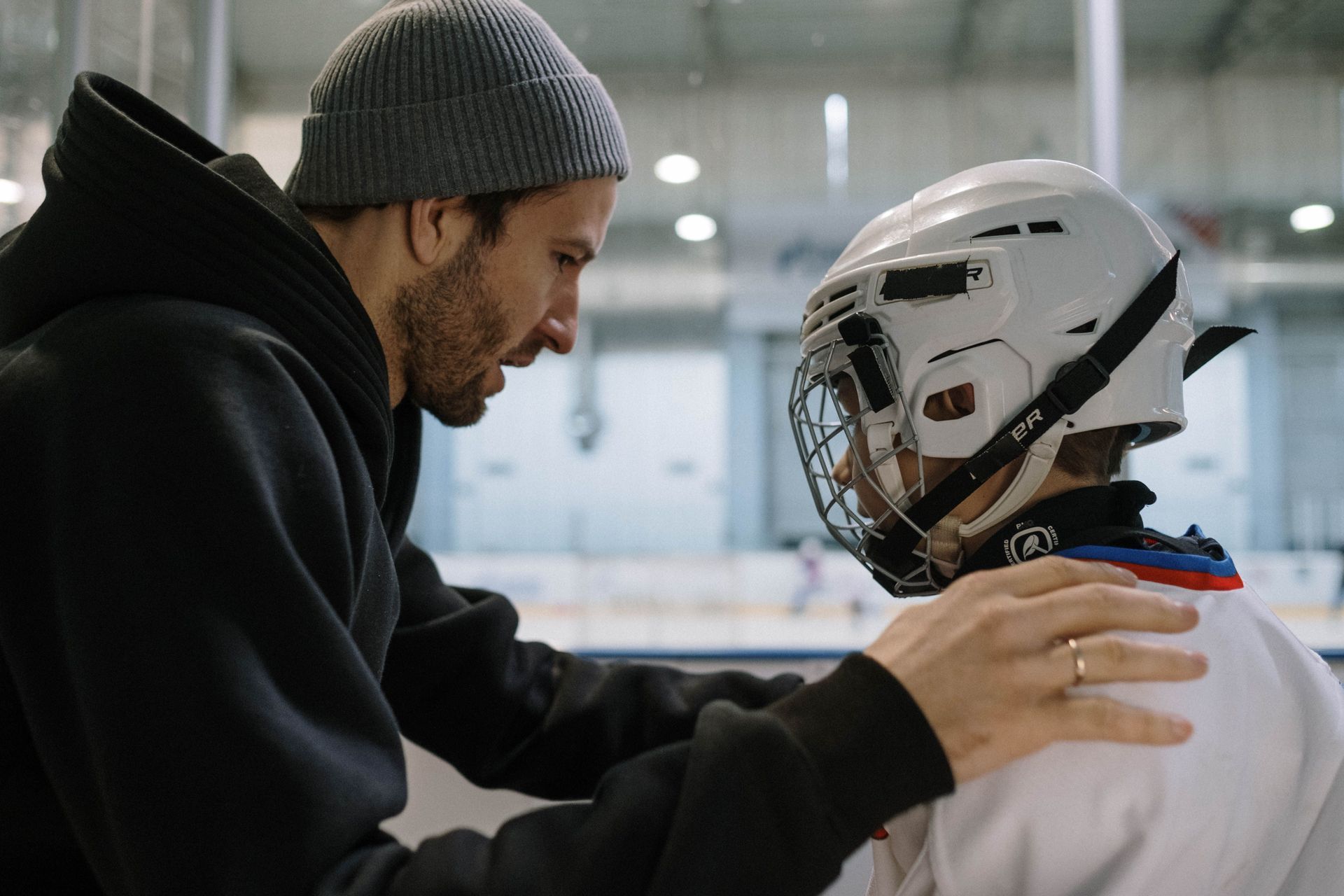 Coach speaking with a hockey player in a rink, hand on shoulder, both in helmets and gear