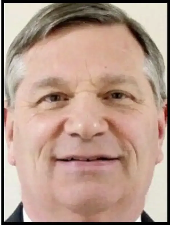 Close-up portrait of a smiling man with short gray hair against a light background